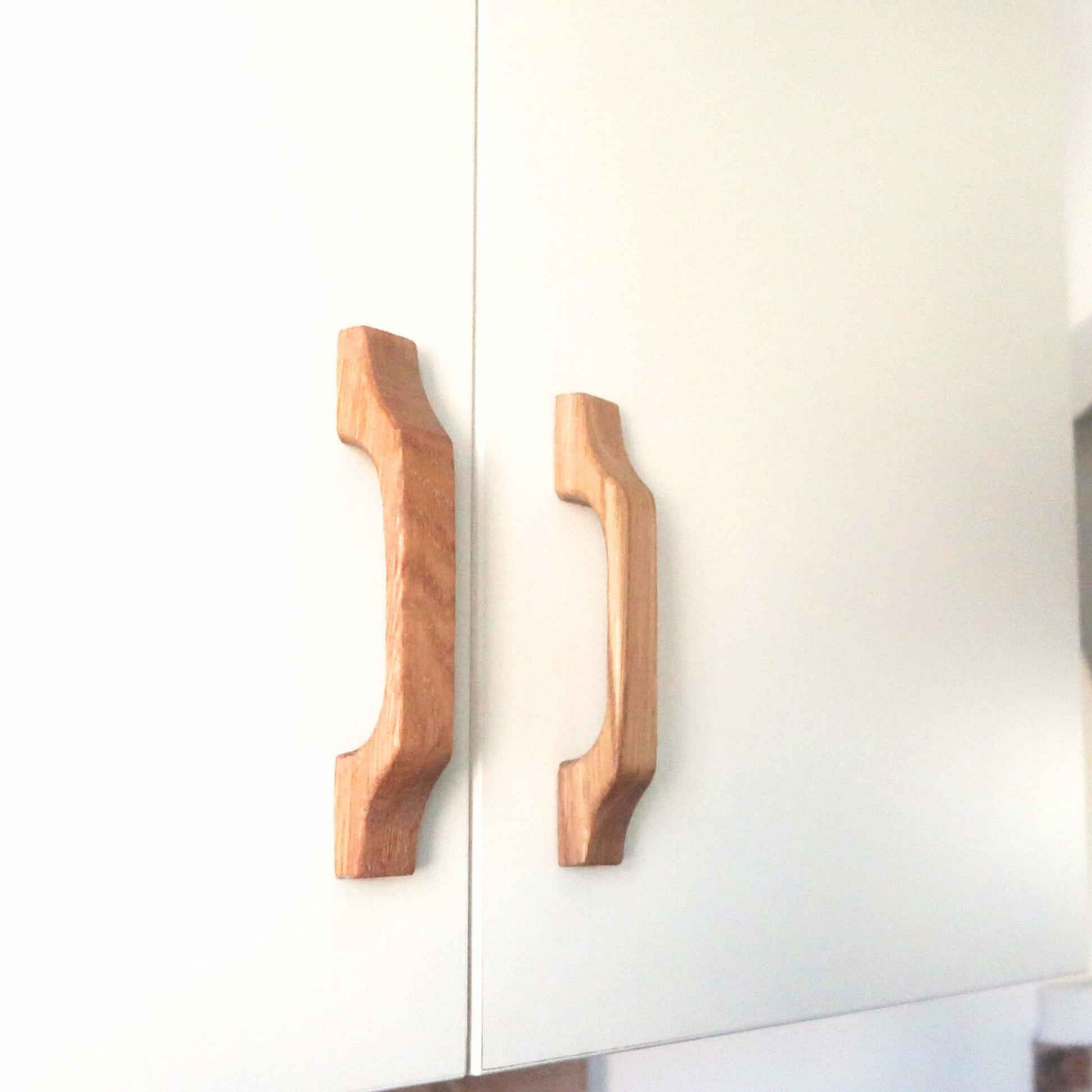 Two contoured oak wood cabinet handles mounted on white doors in natural light
