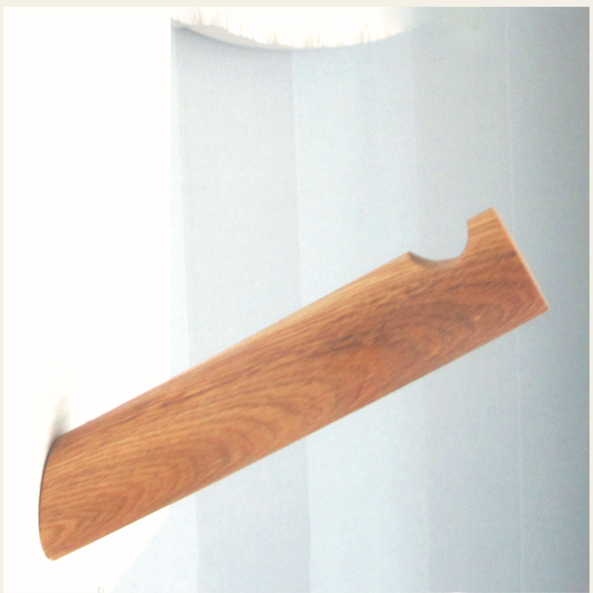 Minimalist oak wall hook with rounded cutout mounted on a light blue wall