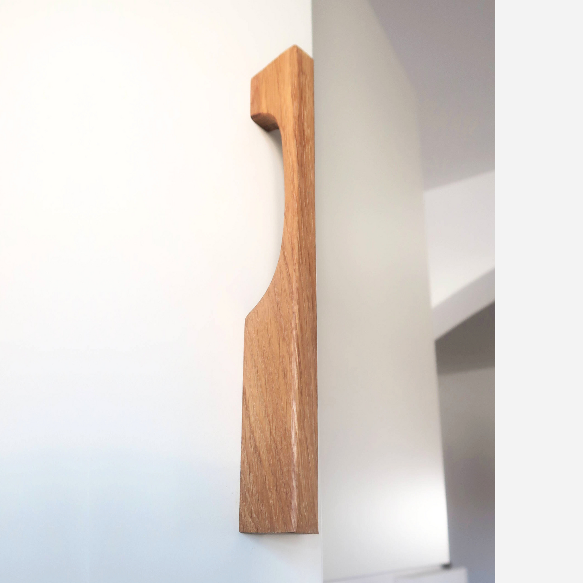A long oak wood cabinet pull mounted on a white door, showcasing its natural wood grain.