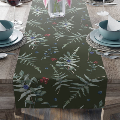 The table runner has a dark green background with a pattern of green leaves, red  and blue berries