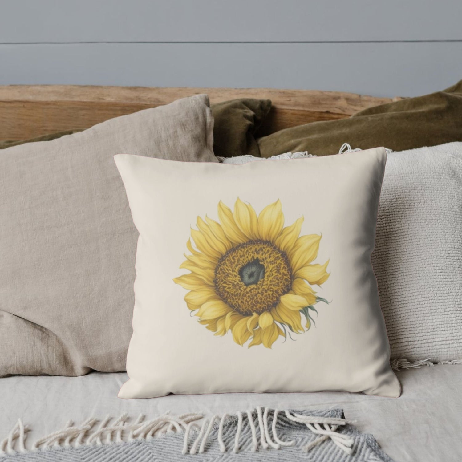 A cozy bed with neutral-colored pillows, featuring a standout throw pillow with a large, detailed sunflower illustration on a beige background.