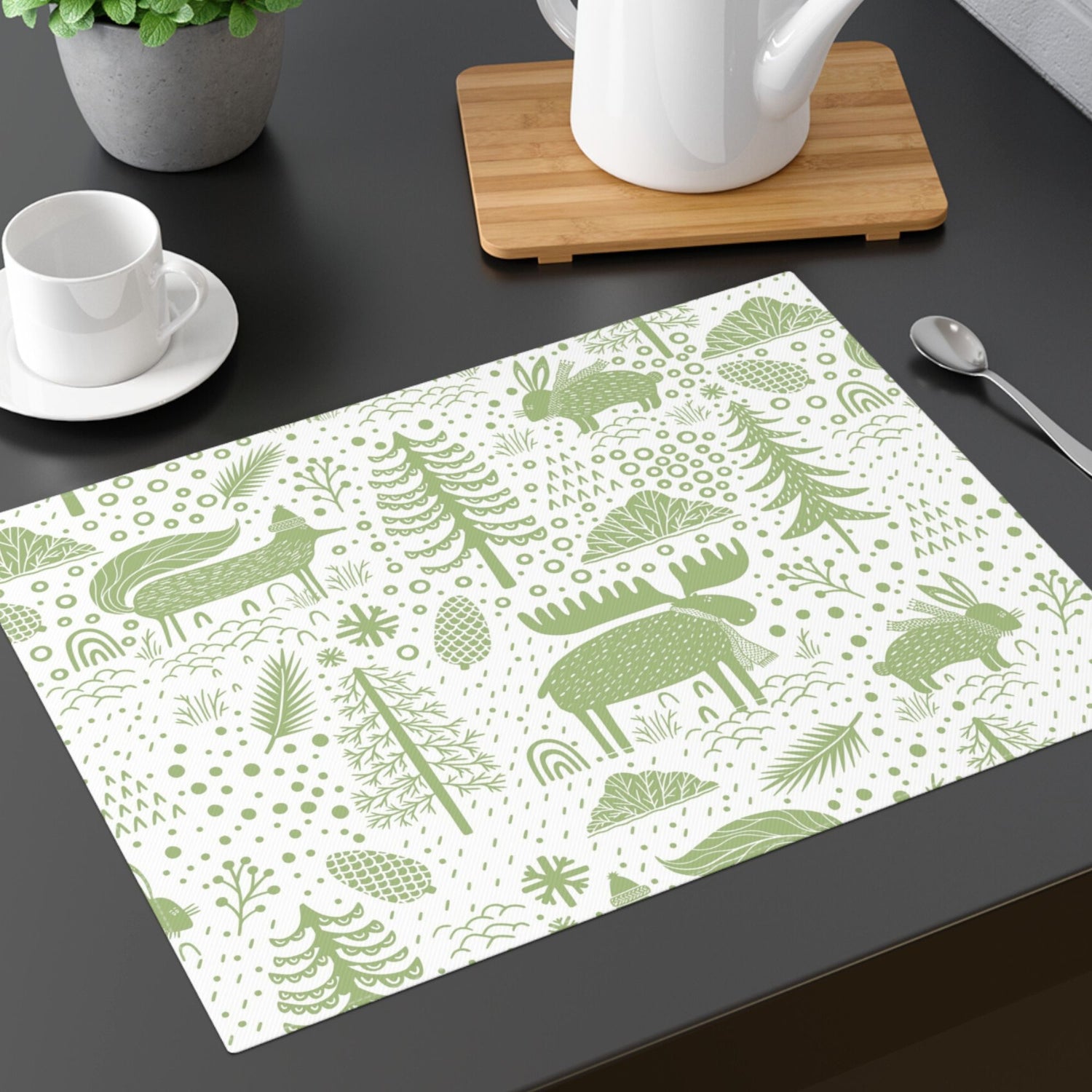a white table placemat featuring a green Scandinavian-inspired pattern of animals, trees, and foliage. 