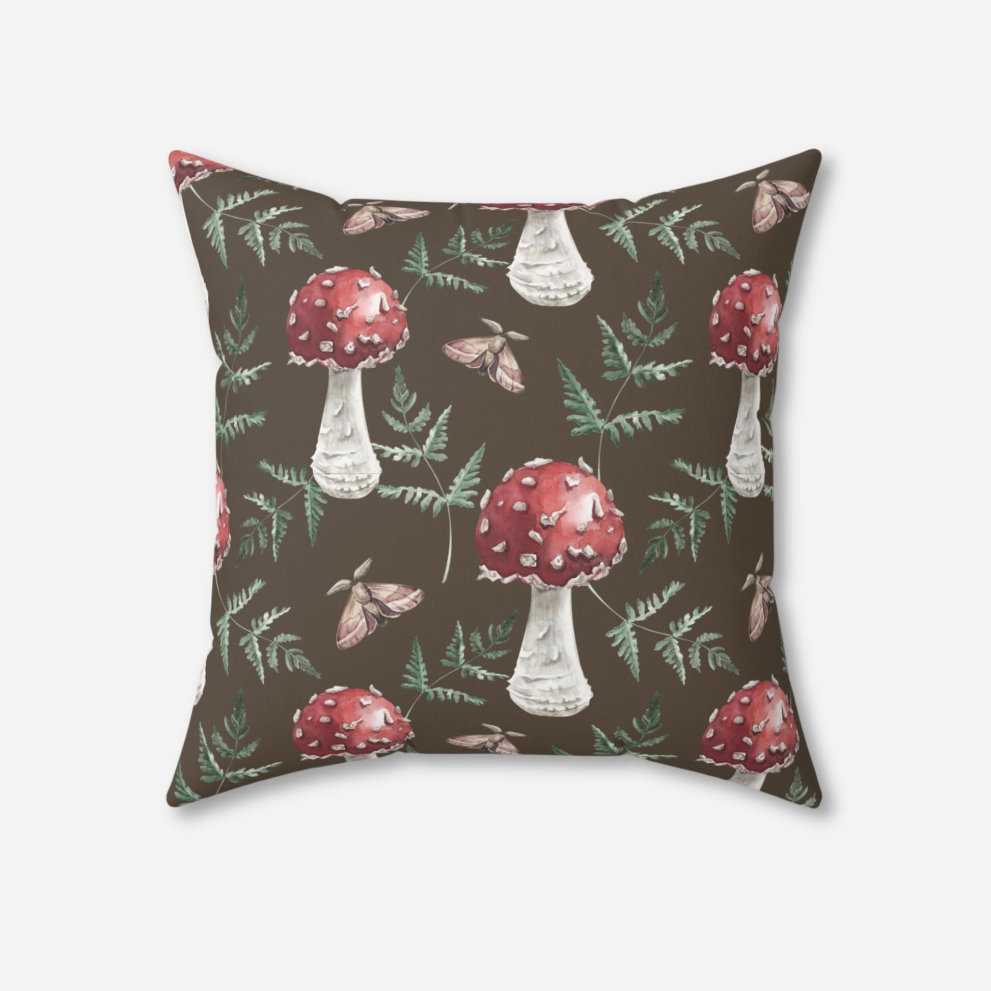 throw pillow adorned with a whimsical design of red mushrooms, green ferns, and moths on a brown background.