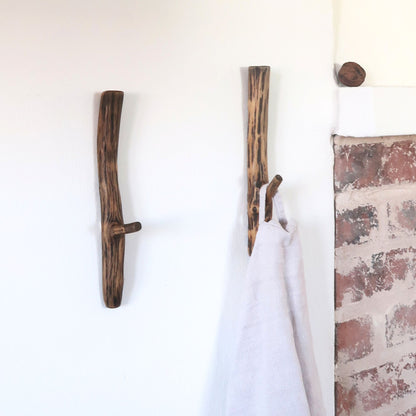 Wooden antler-style hooks on a white wall with a brick-patterned corner.