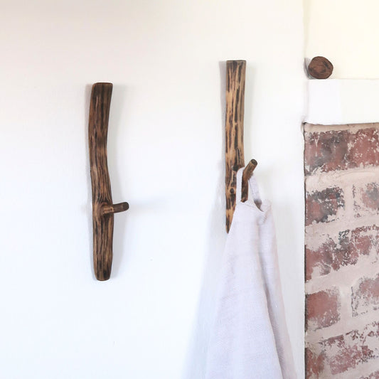 Wooden antler-style hooks on a white wall with a brick-patterned corner.