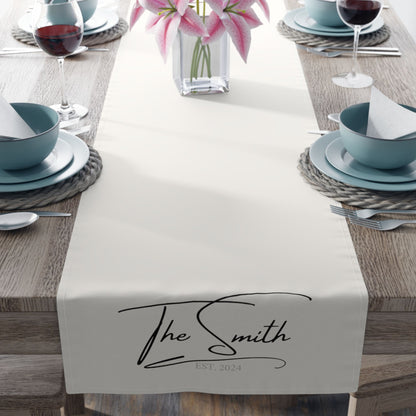 Elegant dining setup with a personalized table runner that reads "The Smith" and "EST. 2024," adorned with pink lilies and set with blue dishware.