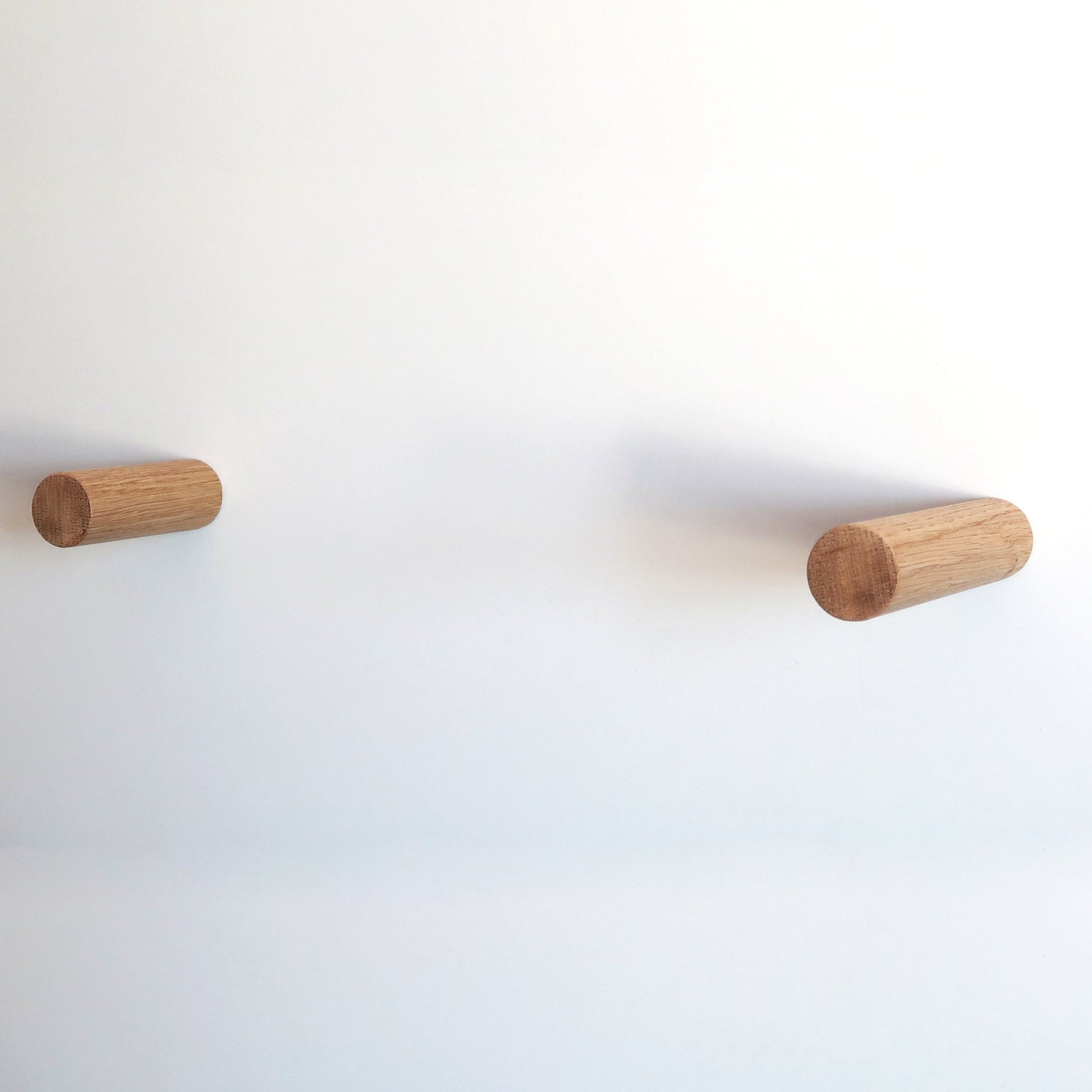 Two cylindrical wooden pegs mounted on a plain white wall, spaced apart horizontally.