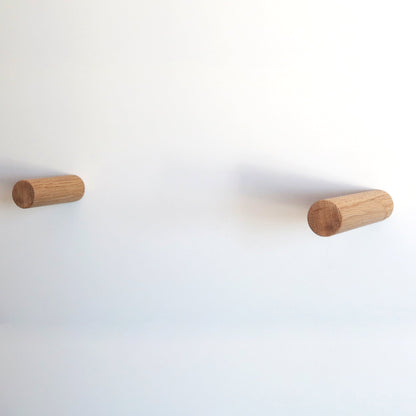 Two cylindrical wooden pegs mounted on a plain white wall, spaced apart horizontally.
