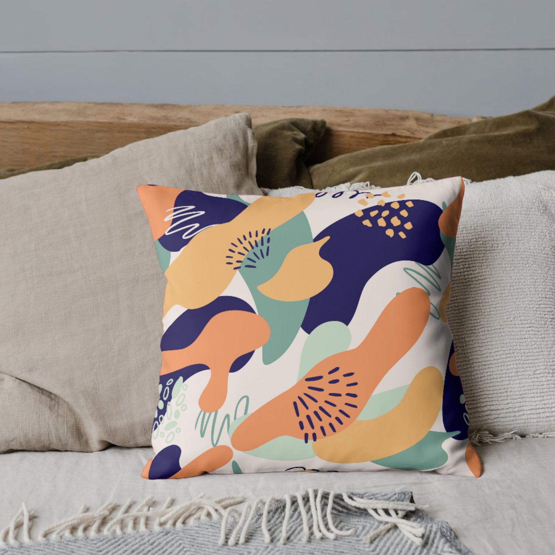 A square pillow showcasing a colorful abstract pattern with organic shapes in orange, navy, green, and cream, giving a playful and artistic vibe.