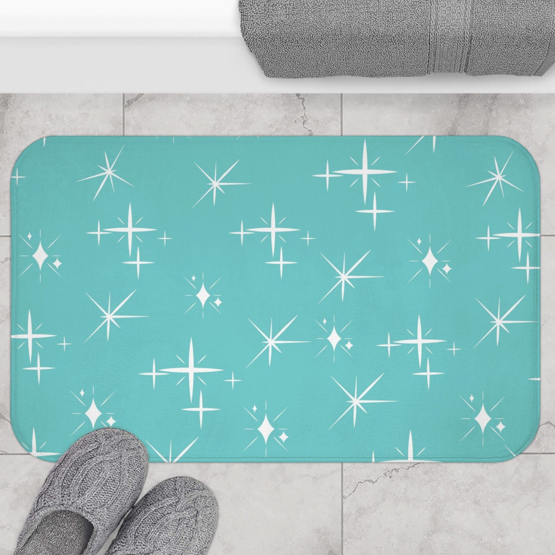 Bathroom mat with a teal background and white starburst pattern, placed on a gray tiled floor.