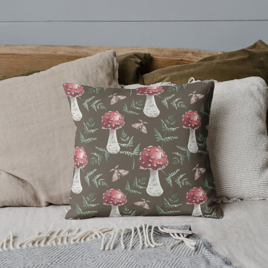 A cozy bed with neutral-colored pillows, featuring a throw pillow with a brown background and a pattern of red-capped mushrooms, ferns, and moths.