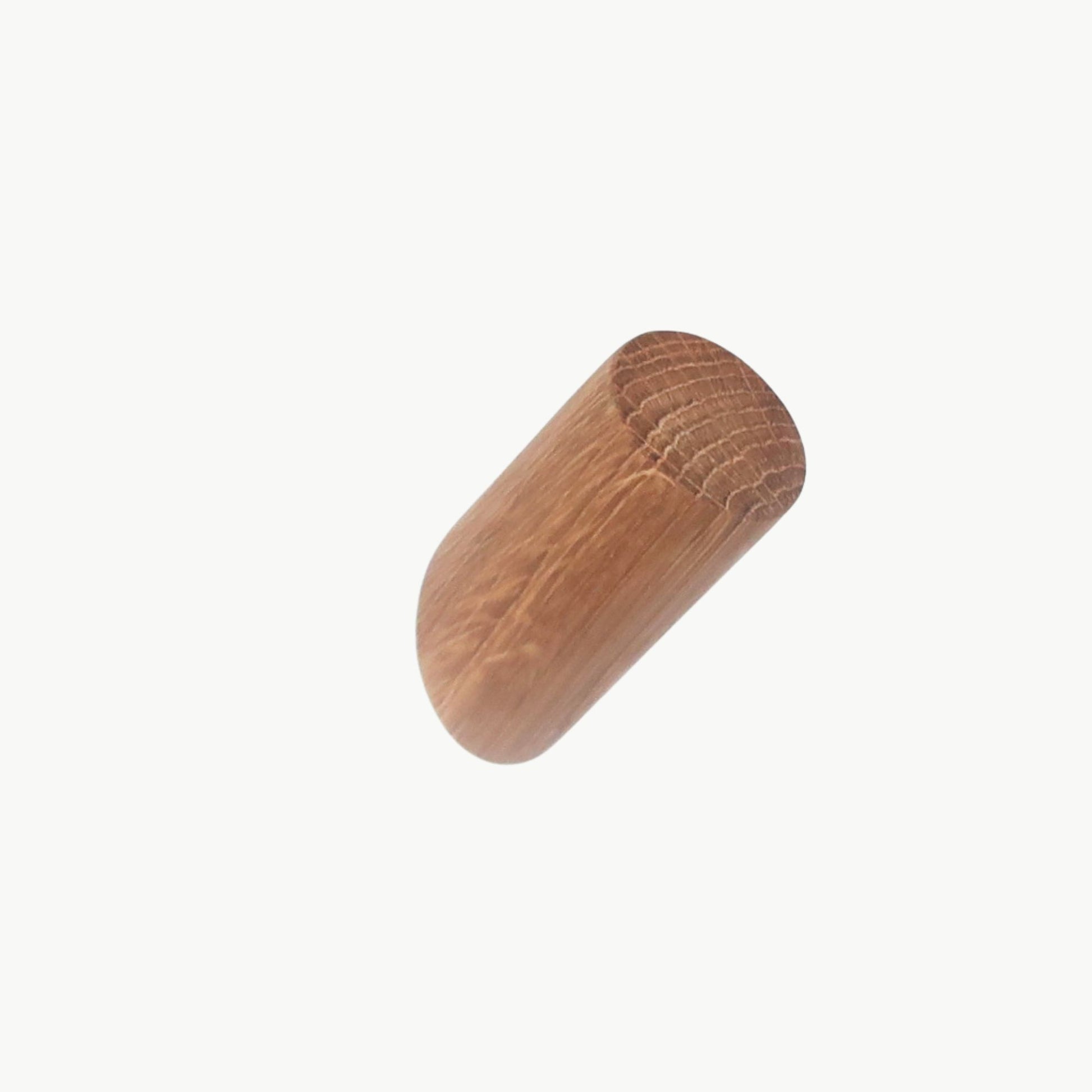 Short solid oak wall hook mounted on white wall, cylindrical wooden peg with natural oil finish.