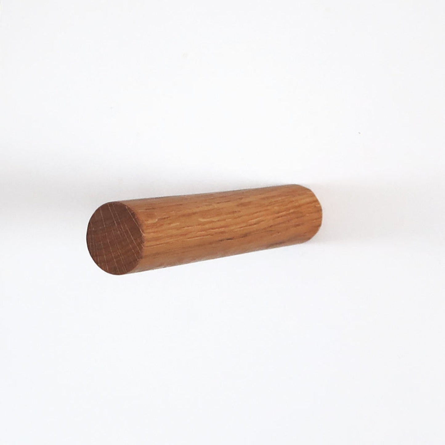 Minimalist wall hook made of solid oak wood, cylindrical shape, front view on white background.