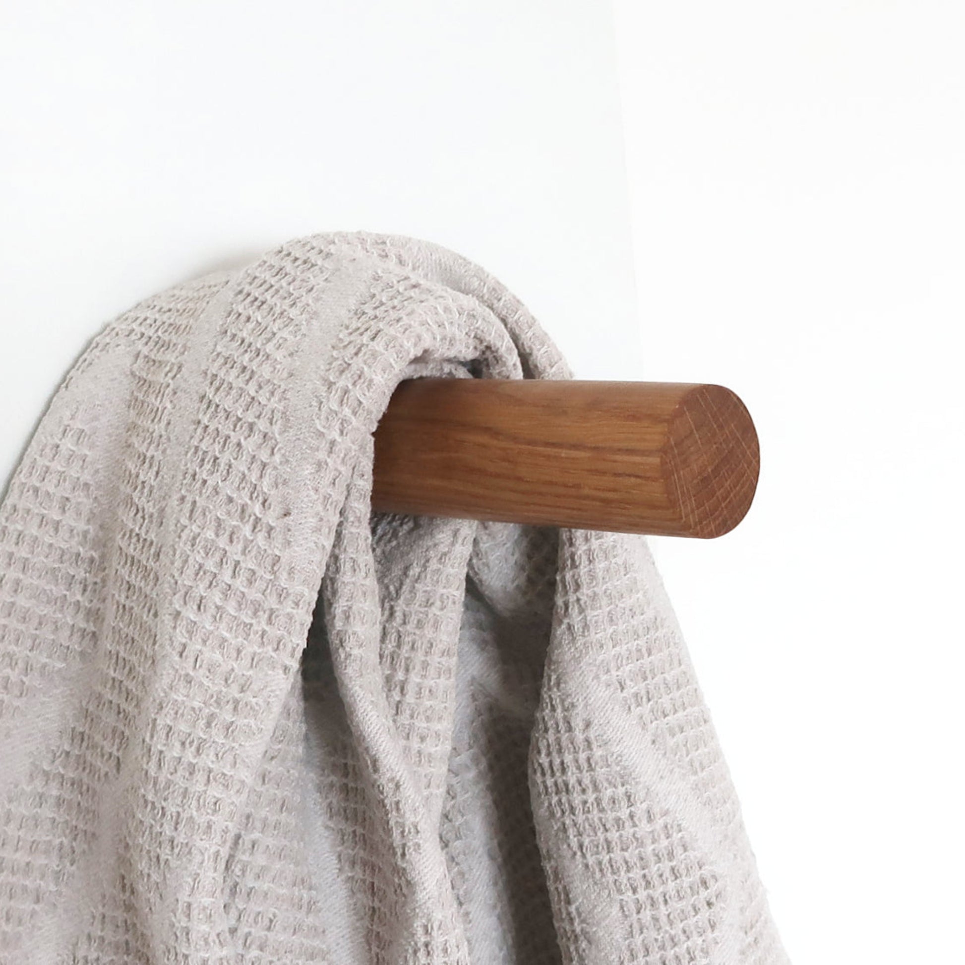 Solid oak wall hook holding a textured towel, natural wood detail for dressing room or sauna entrance.