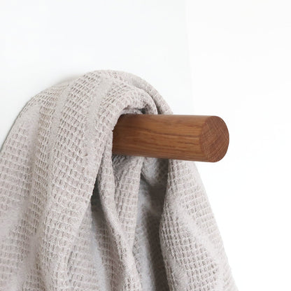 Solid oak wall hook holding a textured towel, natural wood detail for dressing room or sauna entrance.