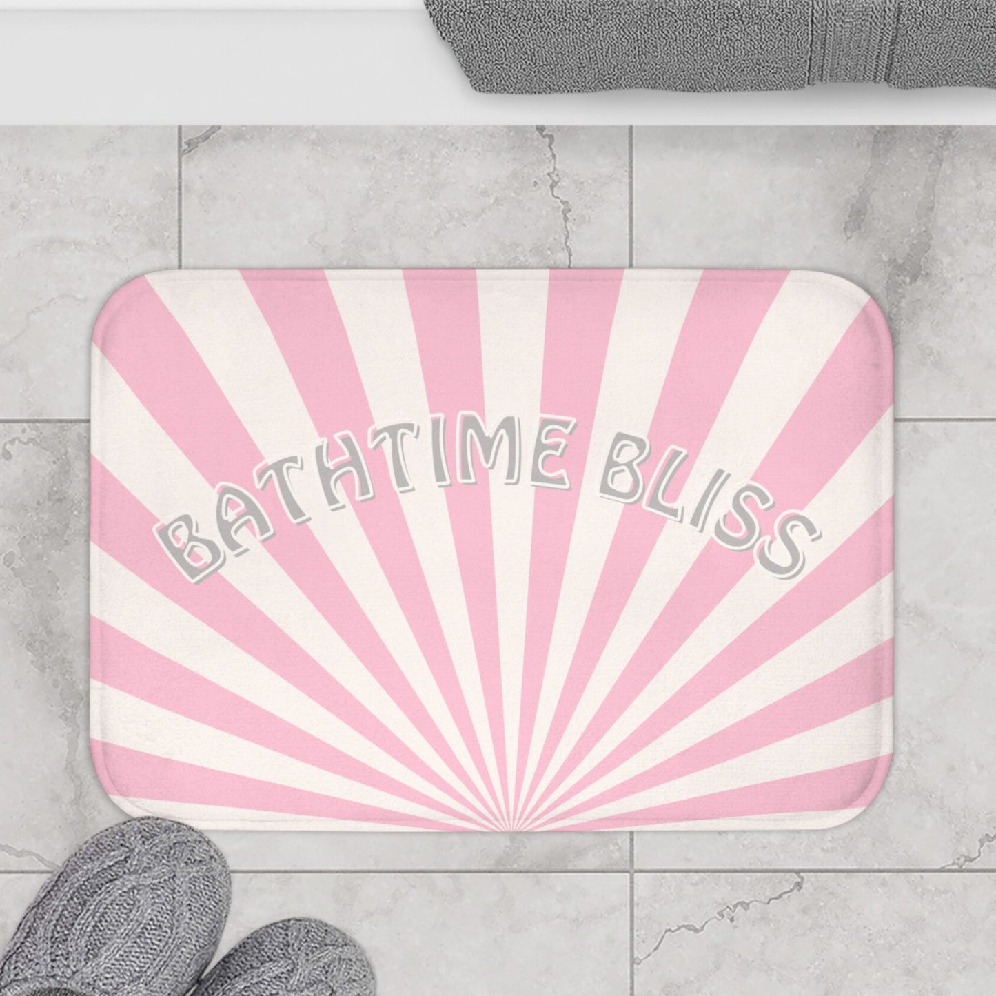 A soft bath mat, featuring a pink and white sunburst design with the phrase "BATHTIME BLISS"