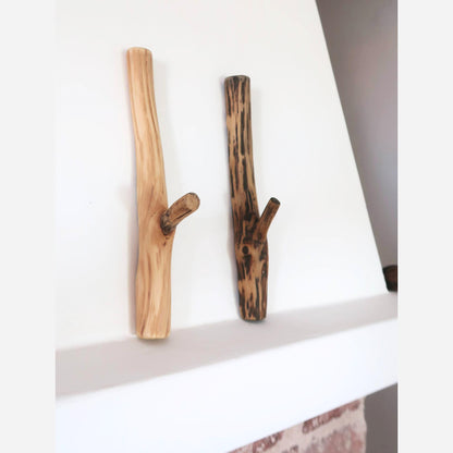 A pair of oak wall hooks, showing a natural, rustic aesthetic with varied textures and shades, attached to a white wall.