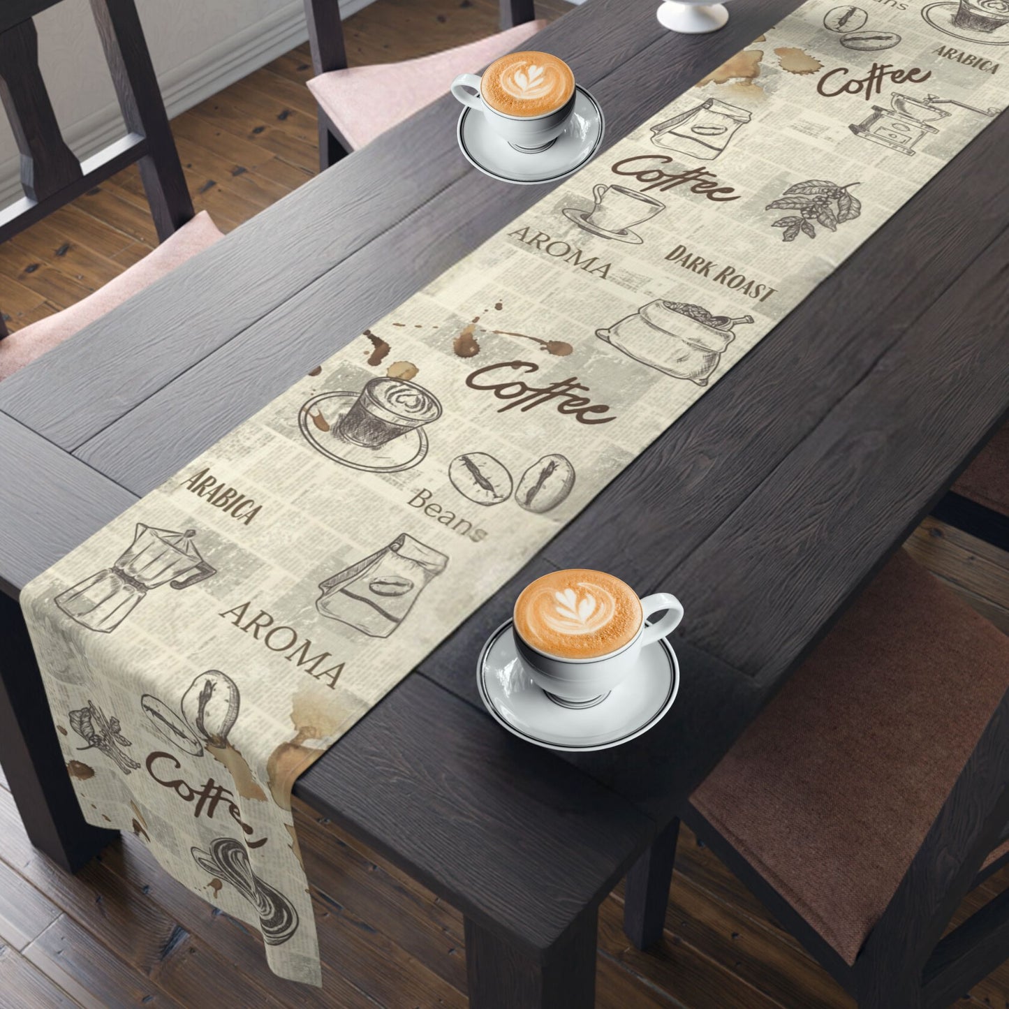 A wooden dining table with a coffee-themed table runner and  cups of cappuccino. The table runner features vintage coffee illustrations and words like "Coffee," "Aroma," and "Dark Roast.