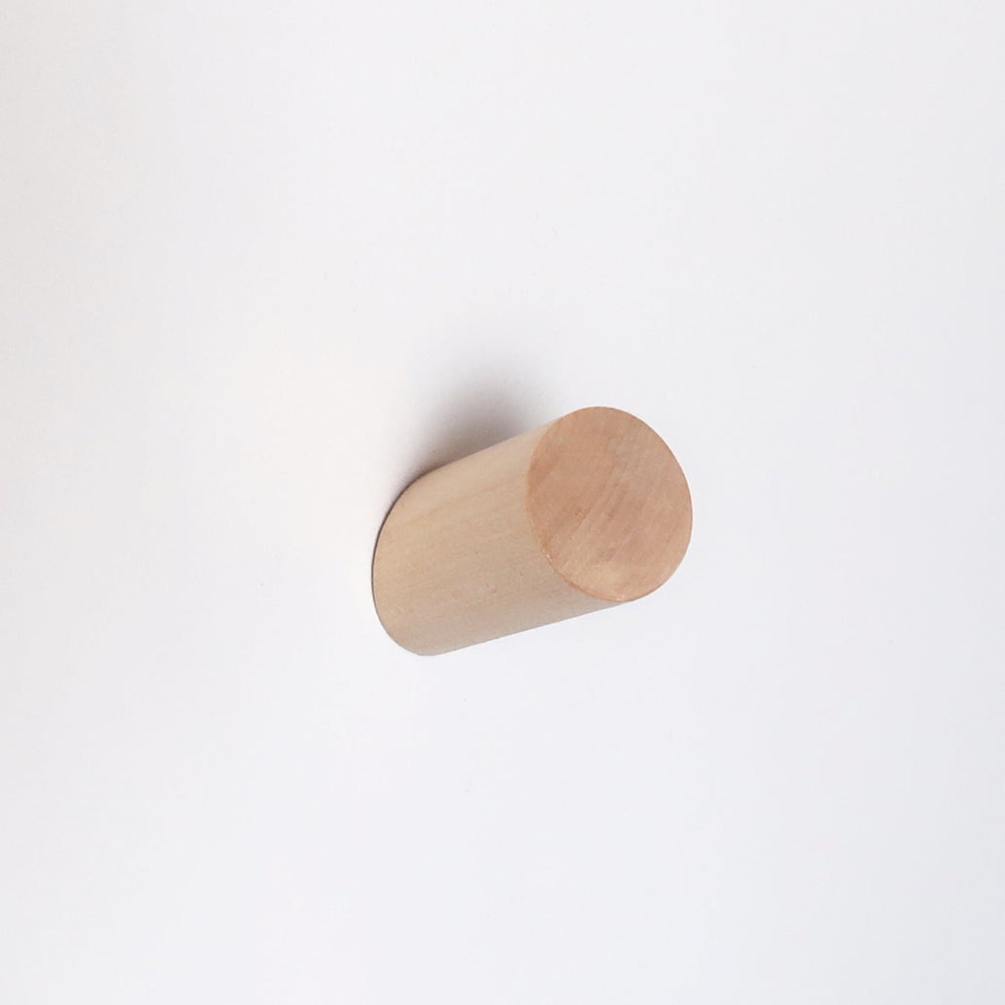 A minimalist light natural wood cylinder wall hook mounted on a plain white wall.