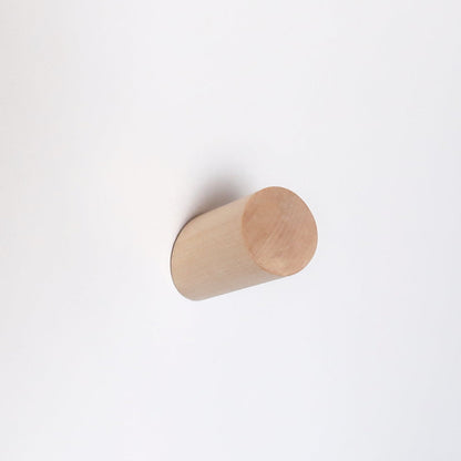 A minimalist light natural wood cylinder wall hook mounted on a plain white wall.