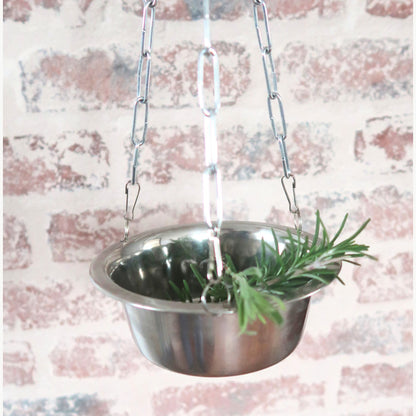 Stainless steel hanging aroma bowl with rosemary against a textured wall background