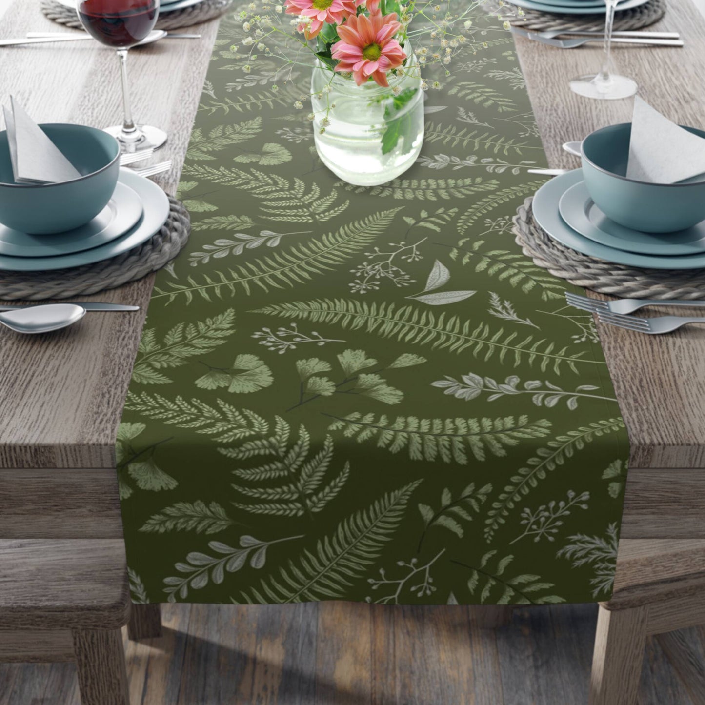 A wooden dining table decorated with a green table runner featuring various fern leaves. 