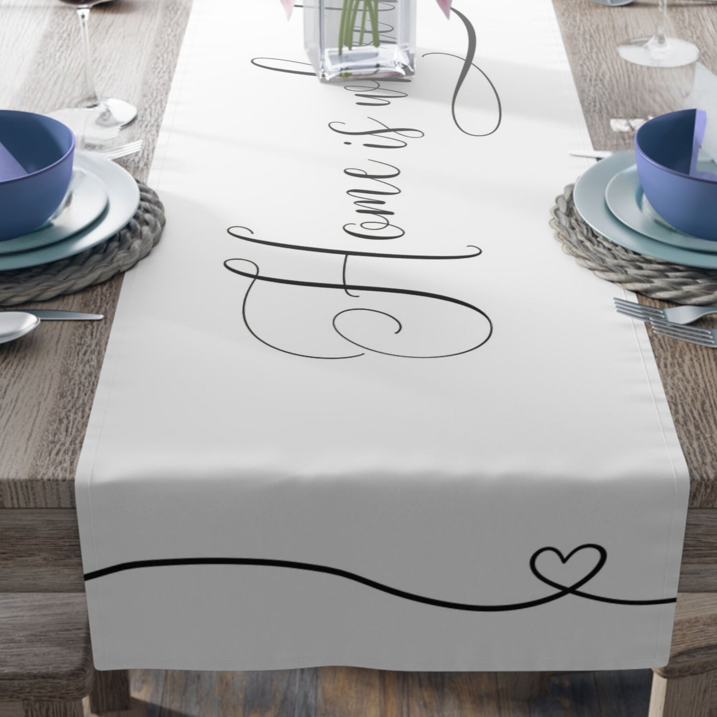 A wooden dining table with a white table runner that reads "Home is where the heart is" in elegant script. 